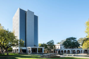 Exterior of a modernist tower surrounded by lower buildings with an arched portico.