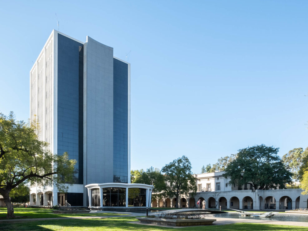 Exterior of a modernist tower surrounded by lower buildings with an arched portico.