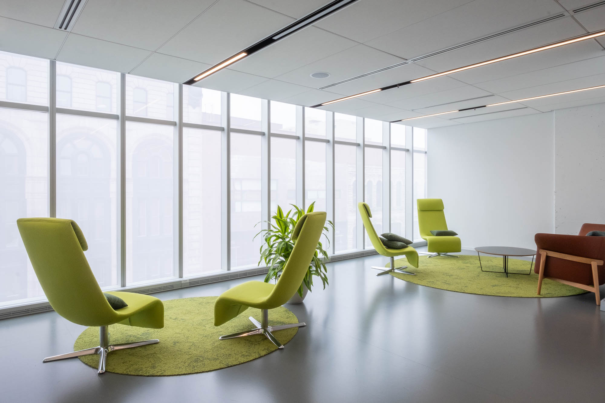 Interior of a contemporary library, a set of lime green coloured sofa chairs in front of floor to ceiling glazing. Neighbouring buildings can be seen through the window.