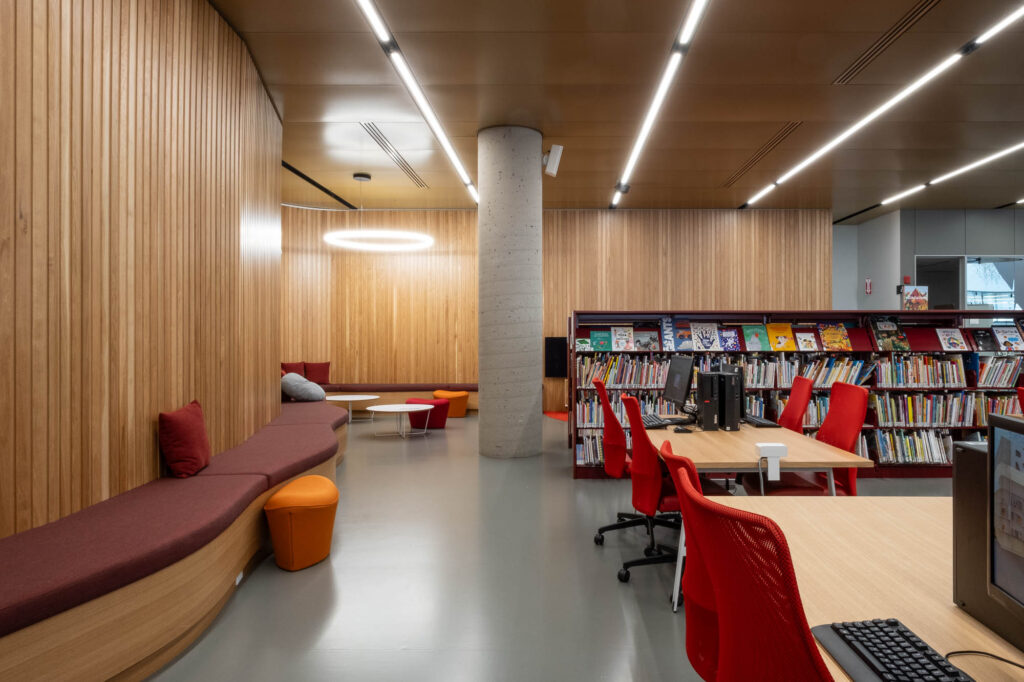 Interior of a contemporary library with wood panelled walls, low bookshelves and computer workstations.