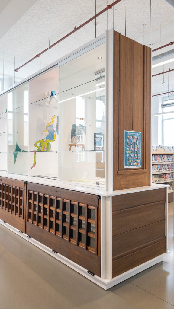 A modern library display case with glass shelves holds artwork and books. Side panels are made with repurposed wooden doors.