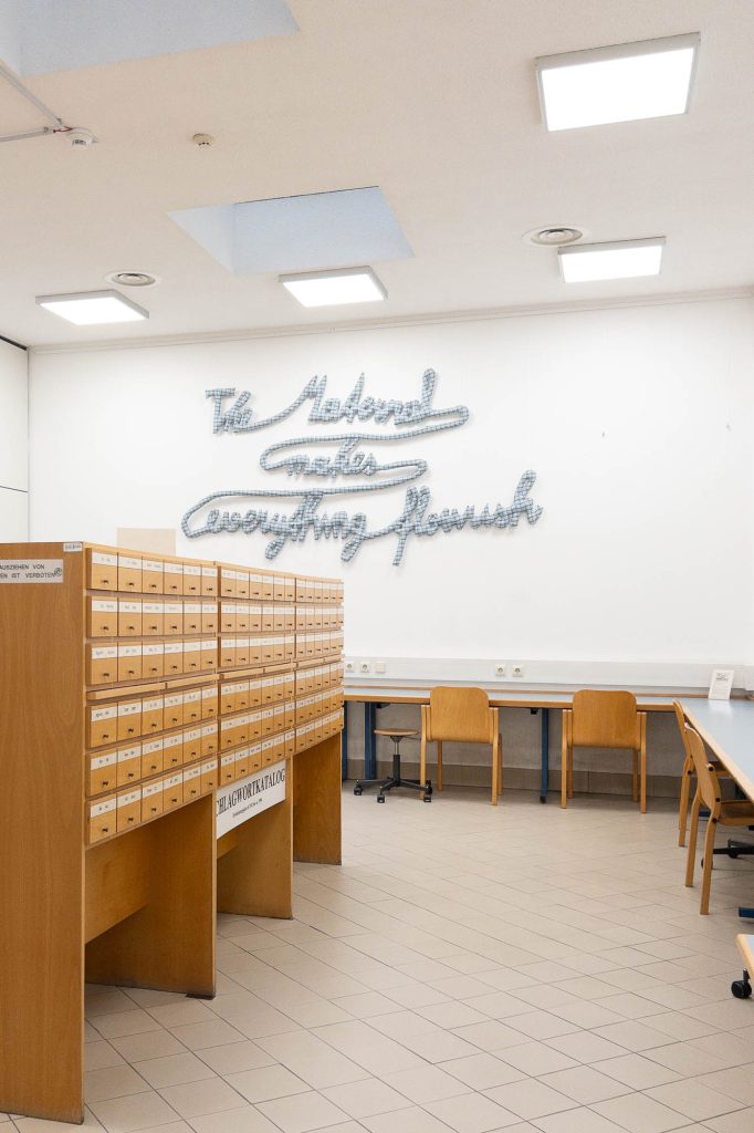A library room with wooden card catalog cabinets. On the wall is an artwork made of fabric displaying the words "The Material makes everything flourish".