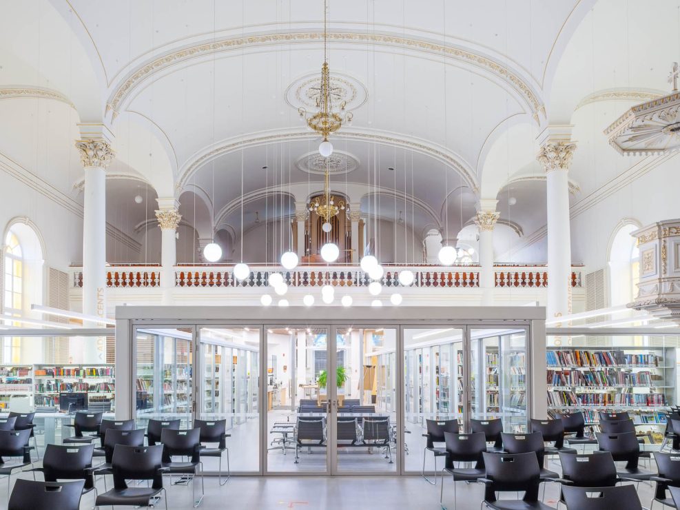 Interior of a church converted to a library. A glass enclosure containing the library is at the back, only occupying part of the church, which can be seen around the library.