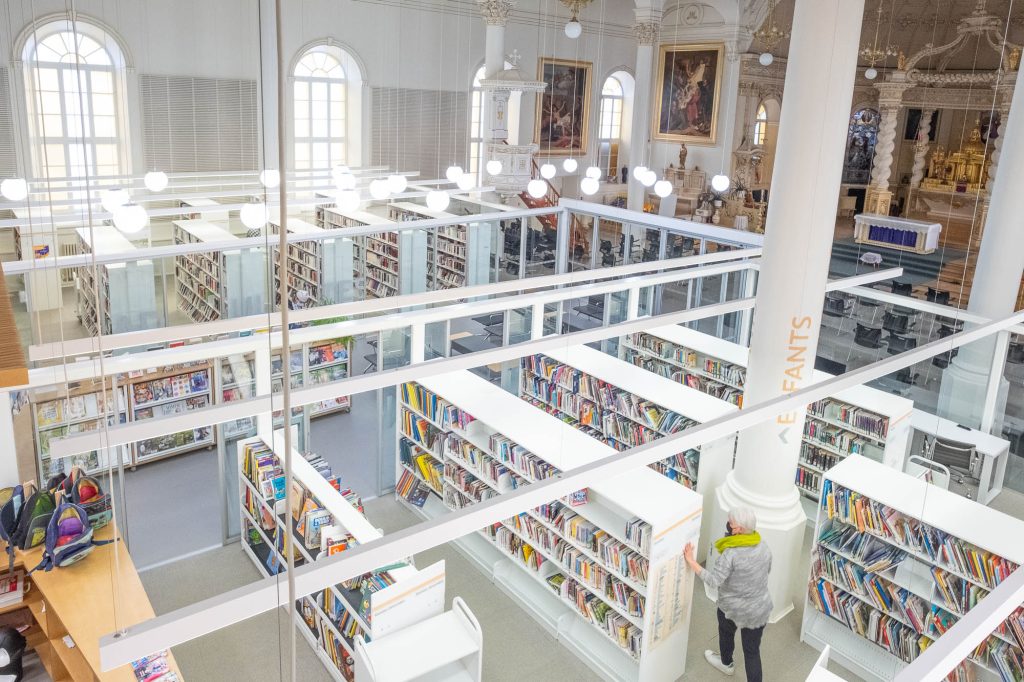 Interior of a church converted to a library. A glass enclosure containing the library is in the forefront, only occupying part of the church, which can be seen at the back.