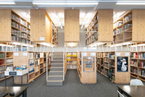 A modern library interior with wooden bookshelves on two levels and a central staircase.
