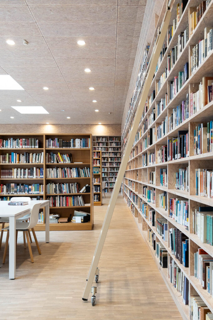 A large library room with floor-to-ceiling wooden bookshelves, a rolling ladder, and a white study table.